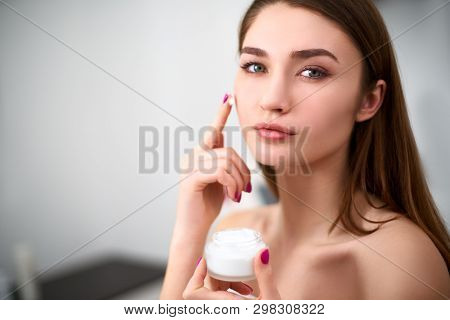 Smiling Young Mixed Race Woman Applying Face Cream On Her Perfect Skin. Model With Flawless Skin Hol