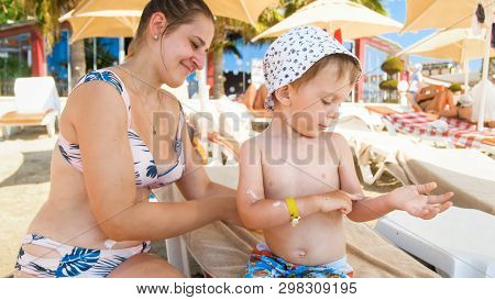Beautiful Young Mother Using Sun Protection Lotion On Her Childs Sking Before Sunbathing At Sea Beac