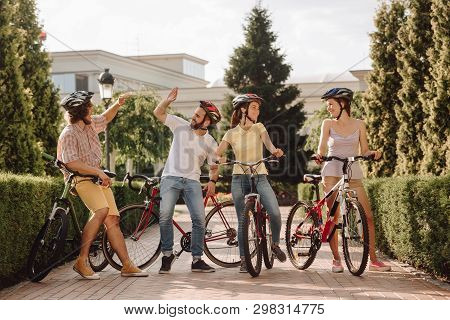 Group Of Cyclists Having Fun Outdoors. Two Young Modern Men Giving Each Other High Five While Restin