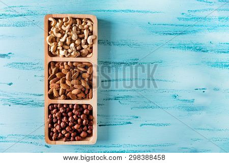 Compartmental Dish With Nuts On Blue Wooden Table. Cashew, Hazelnut, Almond.