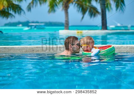 Three year old toddler boy in resort swimming pool eskimo kissing his father. Summer family vacation at Maldives.