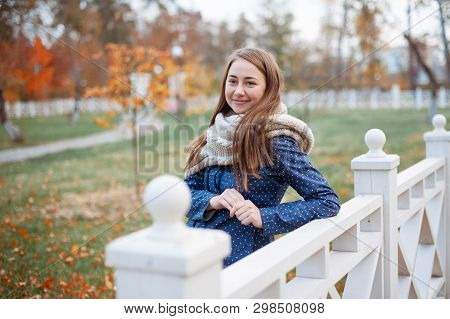 Beautiful Woman Model Poses Outdoor In The Autumn Park With Knitten Gray Scarf