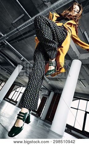 From Below Of Crop Trendy Beautiful Model Wearing Yellow Coat And Patterned Overalls Standing In Und