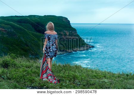 A Young Beautiful Woman With A Blanket In Her Hands Goes To The Top Of The Mountain. General Rear Vi