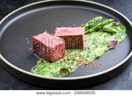 Blanched green asparagus tips with barbecue dry aged wagyu fillet steak and avocado coriander relish as closeup on a modern design plate