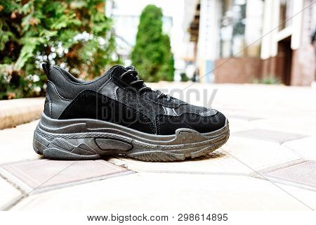 Black Sneakers On Thick Black Soles Against The Background Of Paving Slabs