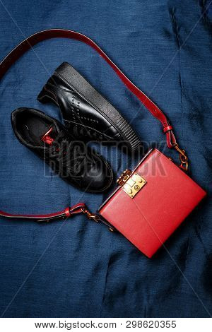 Black Sneakers With Red Tongues And A Red Bag With A Golden Lock On A Blue Woven Background