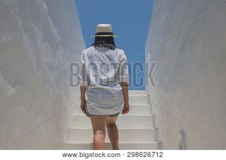 Asian Woman Wear White Shirt And Weave Hat Walking Up On Concrete Stairs In Daylight.