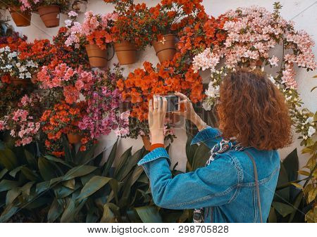 Tourist Woman Taking Photos Of A Street Full Of Flowerpots On The Floor And The Walls, In Spain