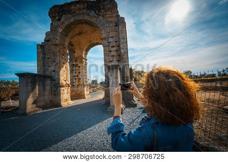 Tourist Woman Taking A Picture With Camera Of The Arch Of Caparra, Ancient Roman City Of Caparra In 