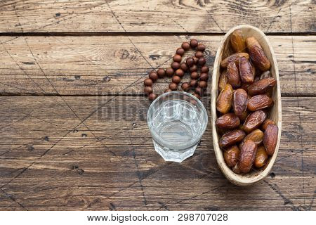 Dried Dates Fruits On A Branch And A Glass Of Water On A Wooden Table, Free Space. Traditional Fast 