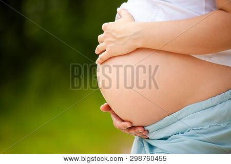 Pregnant Woman Touching Her Big Round Belly With Hands. Sunny Day. Direct Sunlight. Close Up Navel. 