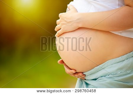 Pregnant Woman Touching Her Big Round Belly With Hands. Sunny Day. Direct Sunlight. Close Up Navel. 