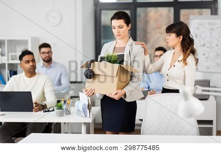 business, firing and job loss concept - colleague seeing off sad fired female employee with box of her personal stuff leaving office
