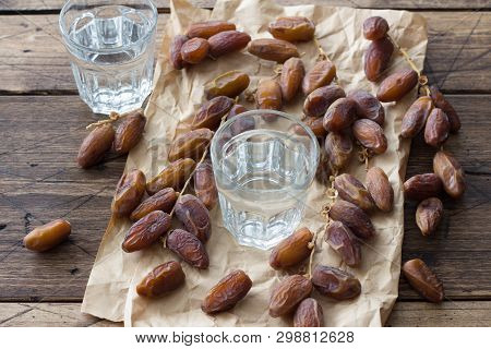 Dried Dates Fruits On A Branch And A Glass Of Water On A Wooden Table. Traditional Fast Breaking, Mu