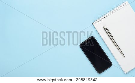 White Notebook With A Metal Pen And A Telephone On A Blue Background. Office Table, Minimal Composit