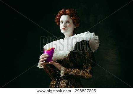 New Taste. Medieval Redhead Young Woman In Golden Vintage Clothing As A Duchess Eating A Fried Potat