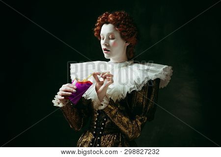 Taste Of Future. Medieval Redhead Young Woman In Golden Vintage Clothing As A Duchess Eating A Fried