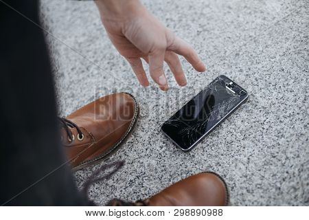 Young Woman Picks Up Her Broken Smartphone With Cracked Screen Glass After Falling.
