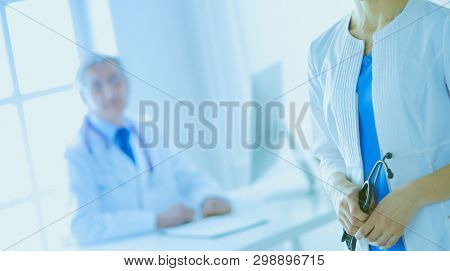 A doctor smiling at the camera with her male colleage in the back of the consulting room in hospital