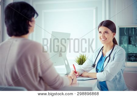 Doctor and patient discussing medical problems in a hospital consulting room. Doc filling in a patient's form