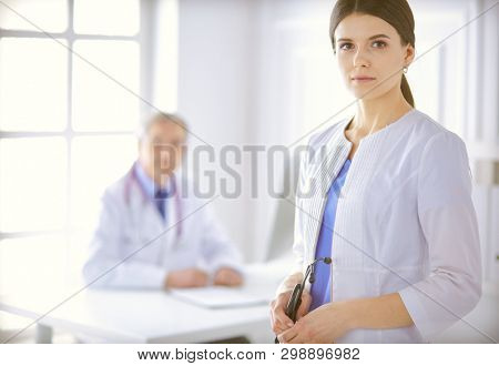 A doctor looking at the camera with her male colleage in the back of the conference room in hospital