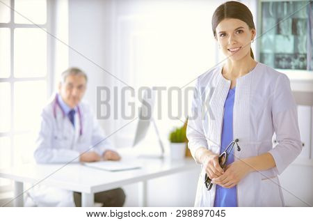 A doctor looking at the camera with her male colleage in the back of the conference room in hospital