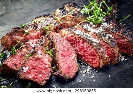 Traditional barbecue dry aged wagyu tomahawk steak sliced salt and herb as closeup on a rustic old black board 