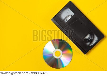 Video Cassette Videotape And Compact Disc On A Yellow Background. Flat Lay Concept.
