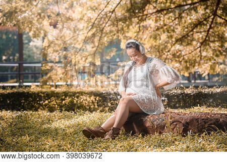 Happy Pregnant Woman Listening To A Music At Park.