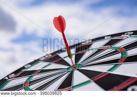 Red Dart Arrow Hitting In The Target Center Of Dartboard With Blue Sky Background