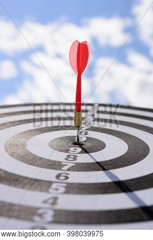 Red Dart Arrow Hitting In The Target Center Of Dartboard With Blue Sky Background