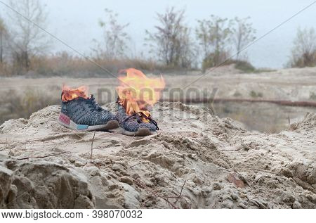 Burning Sports Sneakers Or Gym Shoes On Fire Stand On Sandy Beach Coast. Athlete Burned Out. Physica