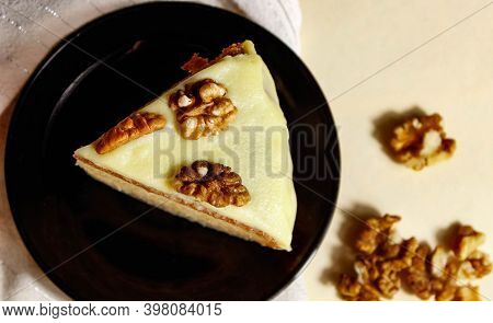 Sponge Cake With Walnuts And Light Cream On A Black Saucer. Top View, Selective Shot.