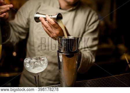 Barman Carefully Pours Drink From Metal Jigger Into Shaker On Bar Counter