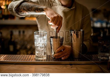 Male Bartender Prepares Cocktail In Shaker Cup Using The Muddler