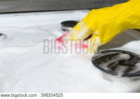 Woman's Hand In Glove Cleaning Gas Stove With Sponge With Foam. Copious Foam From Chemical Cleaning 