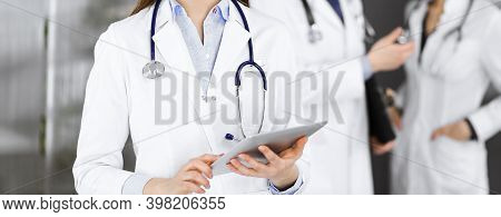 Unknown Woman Doctor Iusing Tablet Computer In Her Hands, While Standing In Clinic. Medicine Concept