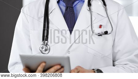 Unknown Male Doctor Iusing Tablet Computer In His Hands, While Standing In Clinic. Medicine Concept 