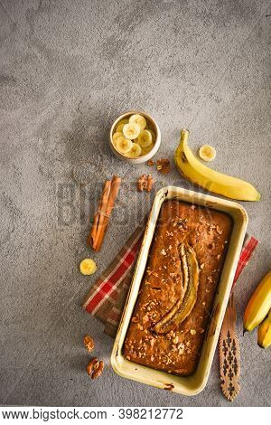 wholegrain Banana bread freshly baked on grey background with banana, cinnamon and nuts. bake shop, loaf, cafe, family baking concepts.
