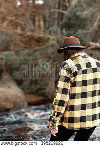 Woman In Yellow Shirt And Hat Walking Along The River In The Autumn Forest