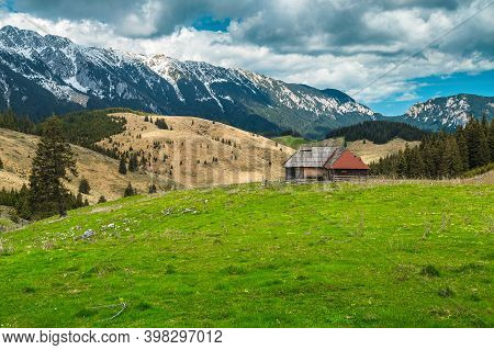 Fantastic Alpine Rural Place With Rickety Wooden Hut And Snowy Piatra Craiului Mountains In Backgrou