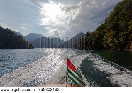Pleasure Boat With Abkhazian Flag Floats On Lake Rizza, View From Behind