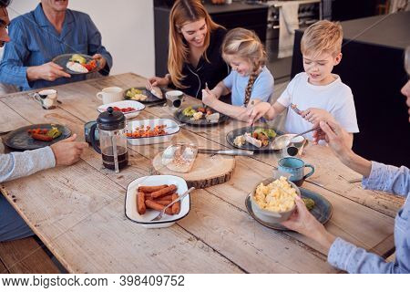 Multi-Generation Family Sitting Around Table At Home In Pyjamas Enjoying Brunch Together