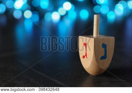 Hanukkah Traditional Dreidel With Letters Gimel And Nun On Table Against Blurred Lights, Closeup. Sp