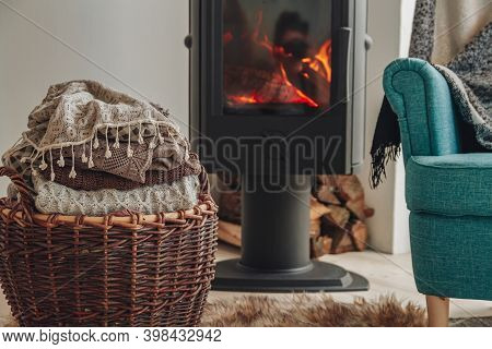 A Stack Of Warm Clothes In A Wicker Basket An Iron Fireplace Wit