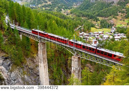 Zermatt, Switzerland. Gornergrat Red Tourist Train On The Bridge In Swiss Alps Summer Panorama