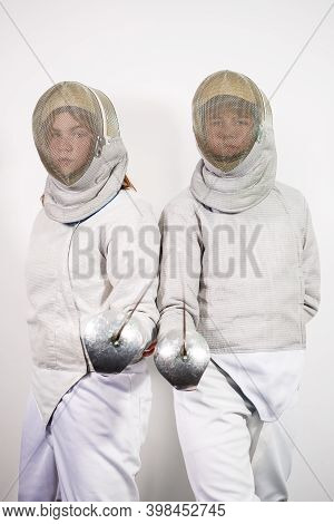 Teenage Girls In Fencing Costumes With Swords In Their Hands Isolated On White Studio Background. Yo