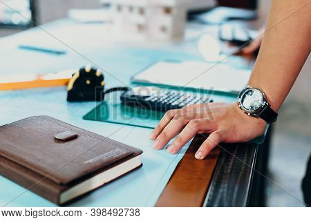Hands Engineer On Table Workplace In Room At Site Construction. Book, Blue Print, Calculater And Too