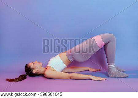 Slim Sporty Woman Lying On Floor In Bridge Pose, Using Fitness Elastic Rubber Band, Wearing Sportswe